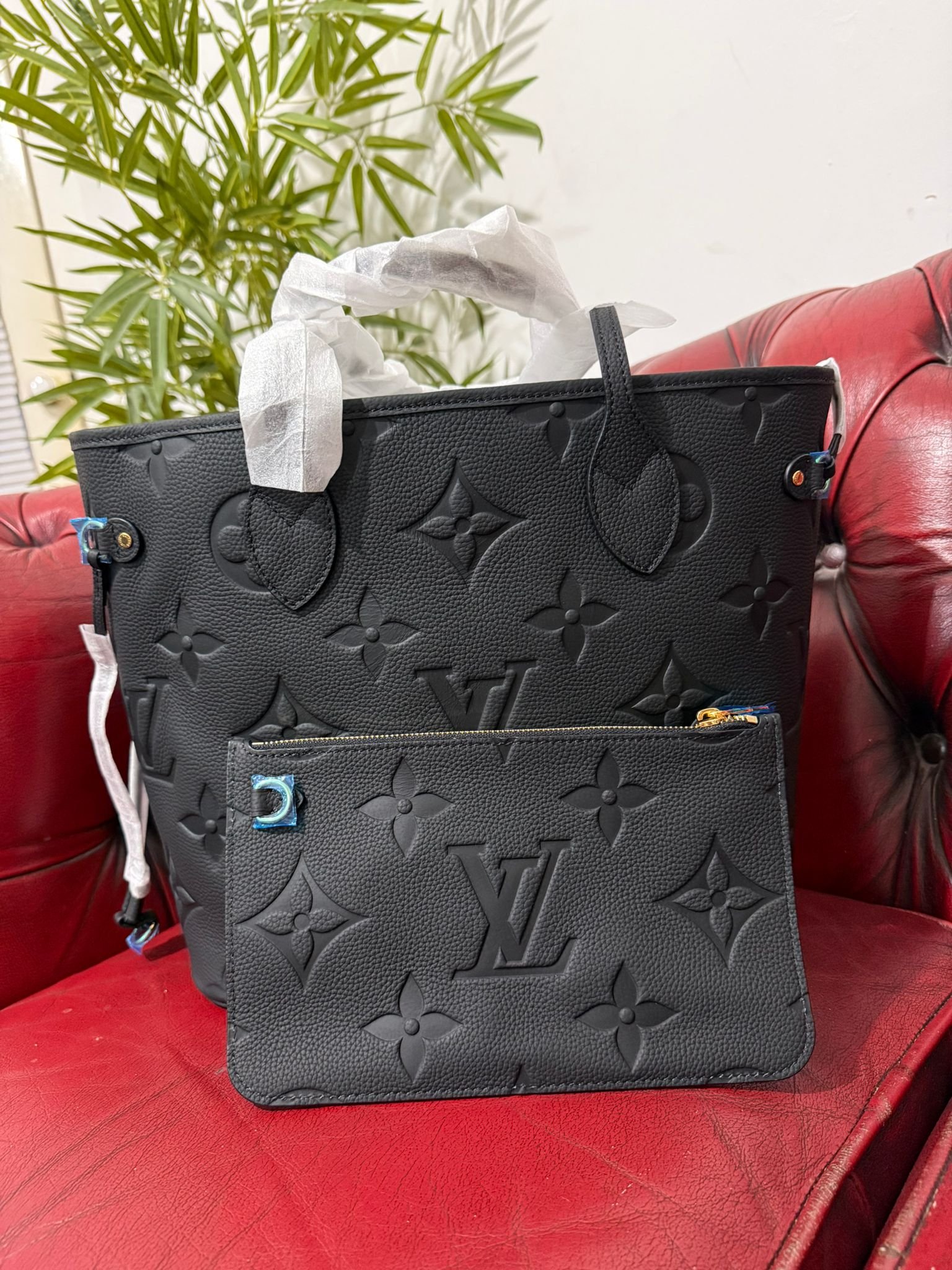 Genuine Leather Neverfull MM Black tote bag with a matching pouch, both featuring embossed monogram pattern.