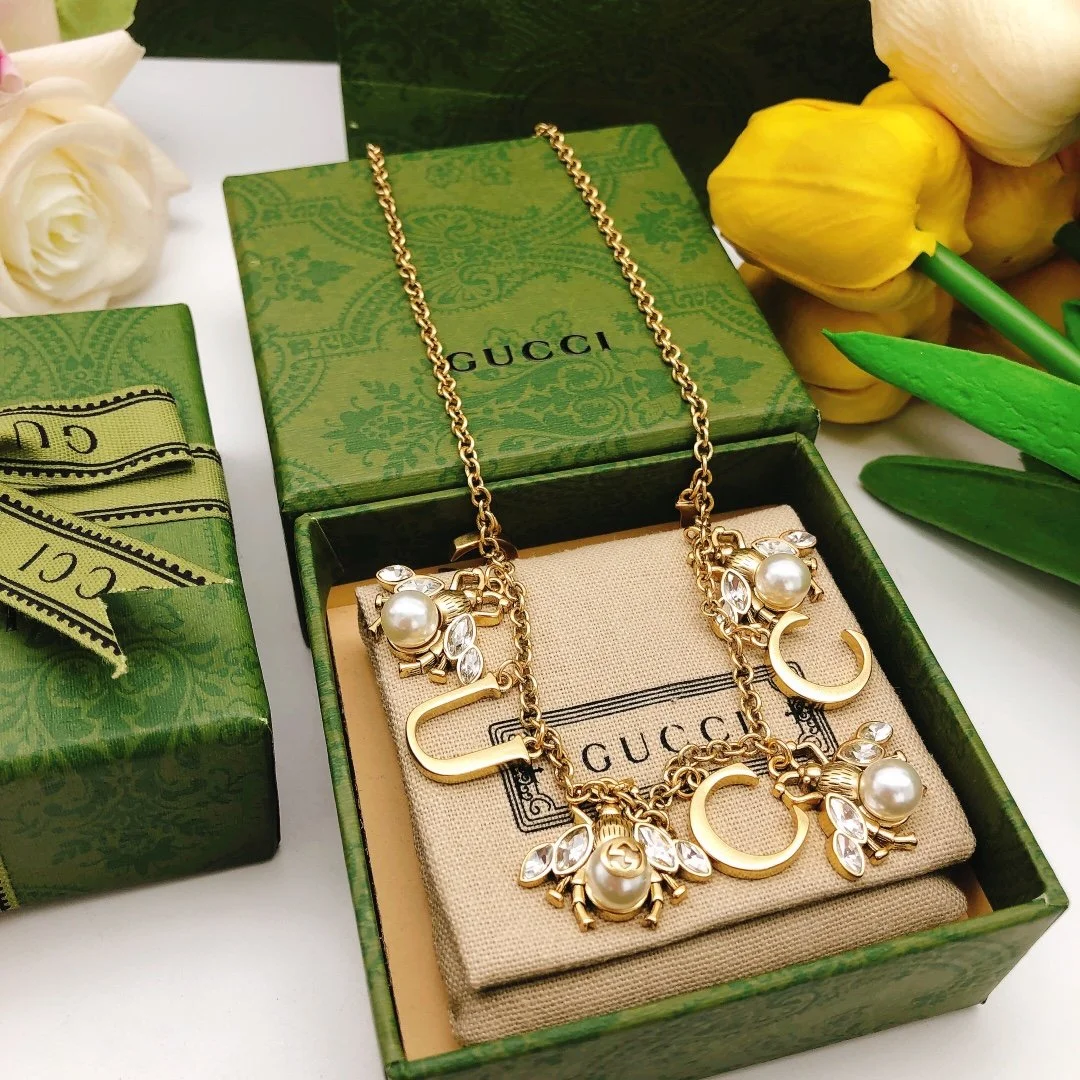 Golden linked chain necklace with metal cutout and bee charms made of pearls and diamonds.